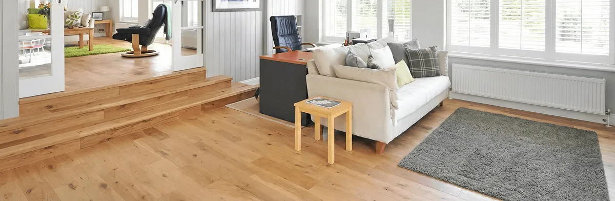 A modern living room with professionally installed laminate flooring, a beige sofa, a small side table, a gray rug, and large windows with white shutters in Chattanooga, TN